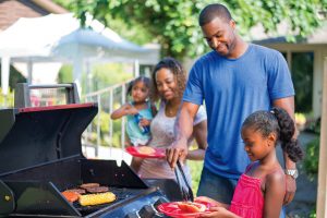 Family cooking hot dogs hamburger and corn on gas grill