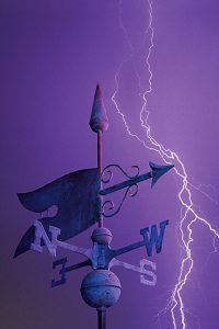 Tip of weather vane against purple sky with lightning bolt