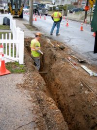 Construction worker in trench on side of road digging gas line